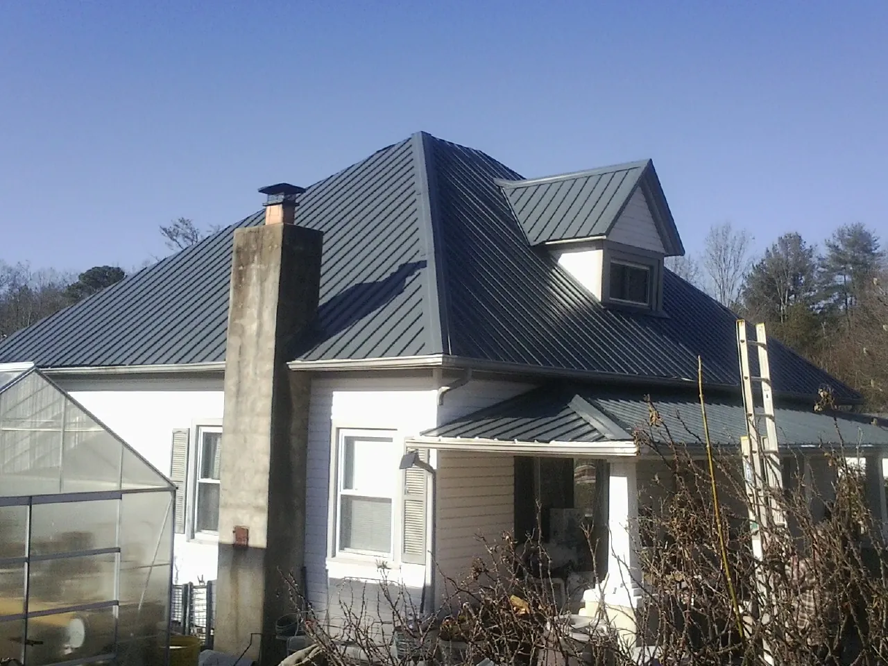 Dark blue standing seam metal roof on a white farmhouse with dormer — Slate & Tile Roof Repair by Roofing Brothers in Teaneck