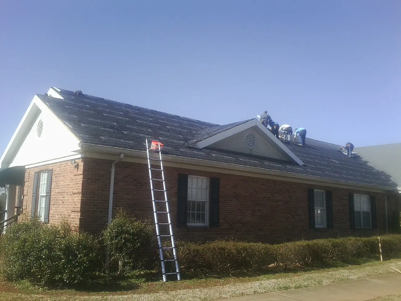 Crew tearing shingles off a brick ranch roof with a ladder set — Emergency Roof Repair work by our crew in Teaneck