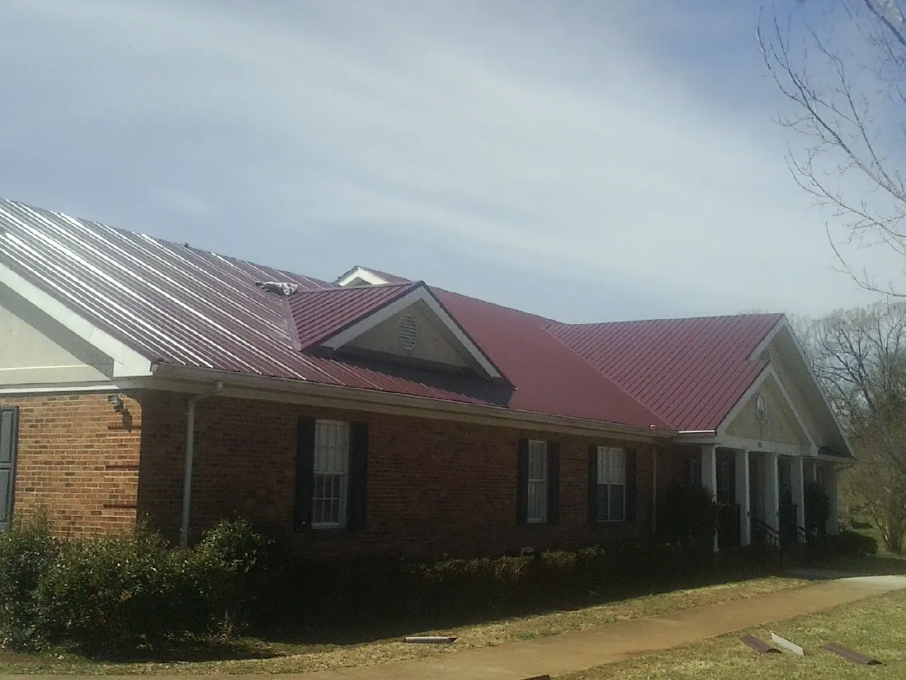 Red metal roof with gabled entries on a long brick building, from a Hail Damage Roof Repair job in Teaneck
