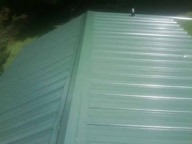 New green metal panels meeting at the ridge of a roof — Flat Roof Repair work by our crew in Teaneck