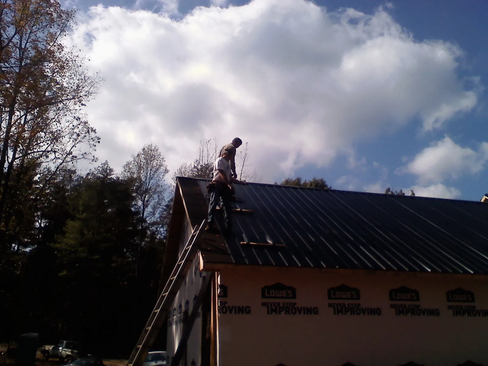 Roofer fastening dark metal panels high against a cloudy sky, from a Roof Inspection job in Teaneck