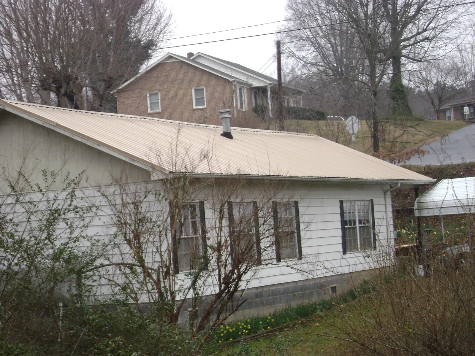 Tan metal roof on a white sided house set into a hillside — Commercial Roofing by Roofing Brothers in Teaneck